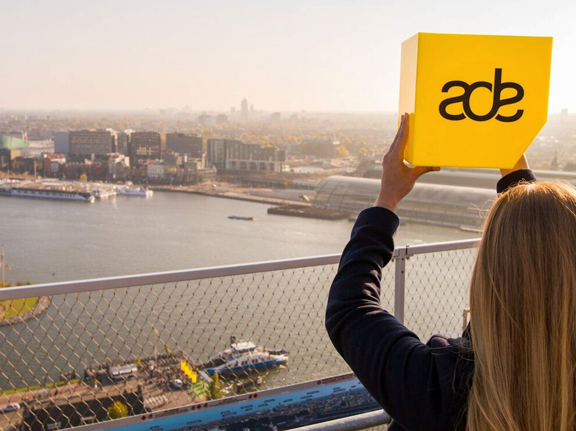 Girl holding ADE sign above bridge of water